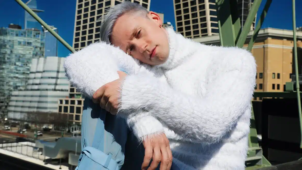 Magnus Riise sits in front of a building with blond hair slightly tinted purple, looking at the camera with his head resting on his shoulder. Picture by Mihailo Sopic